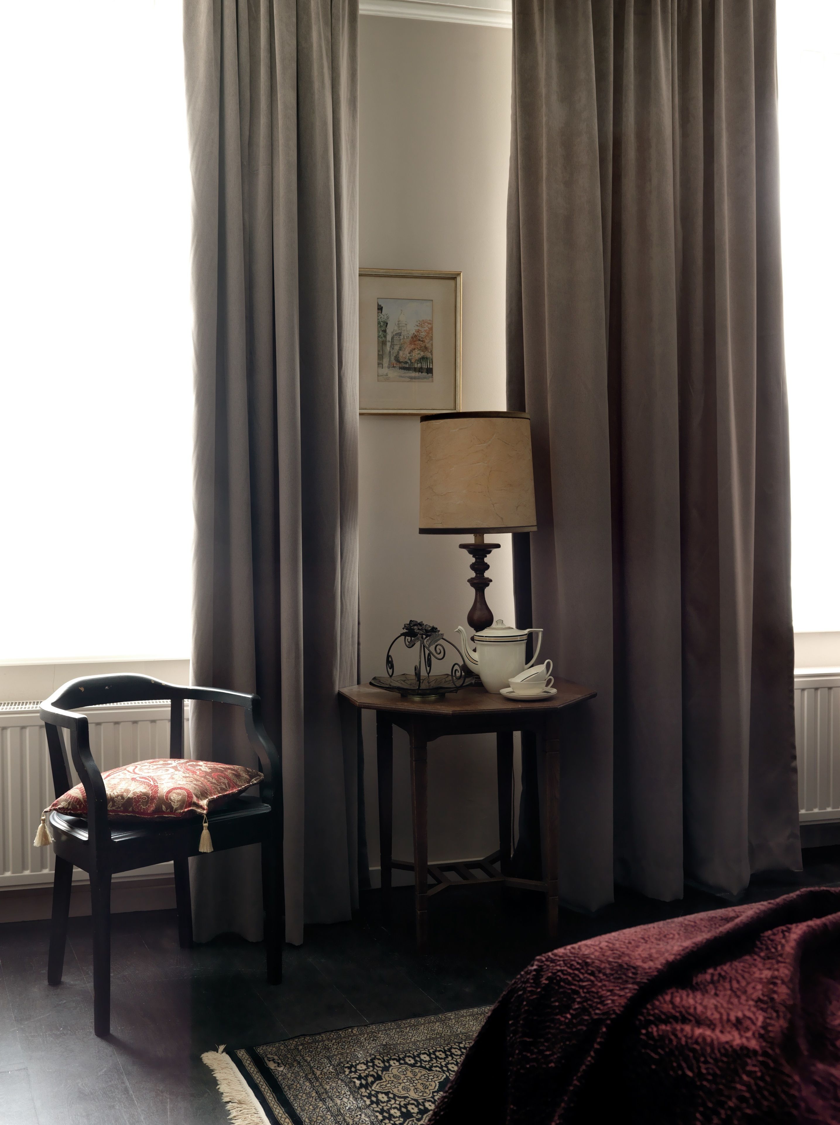 Una habitación con una silla, una mesa con una lámpara y un cuadro en la pared.