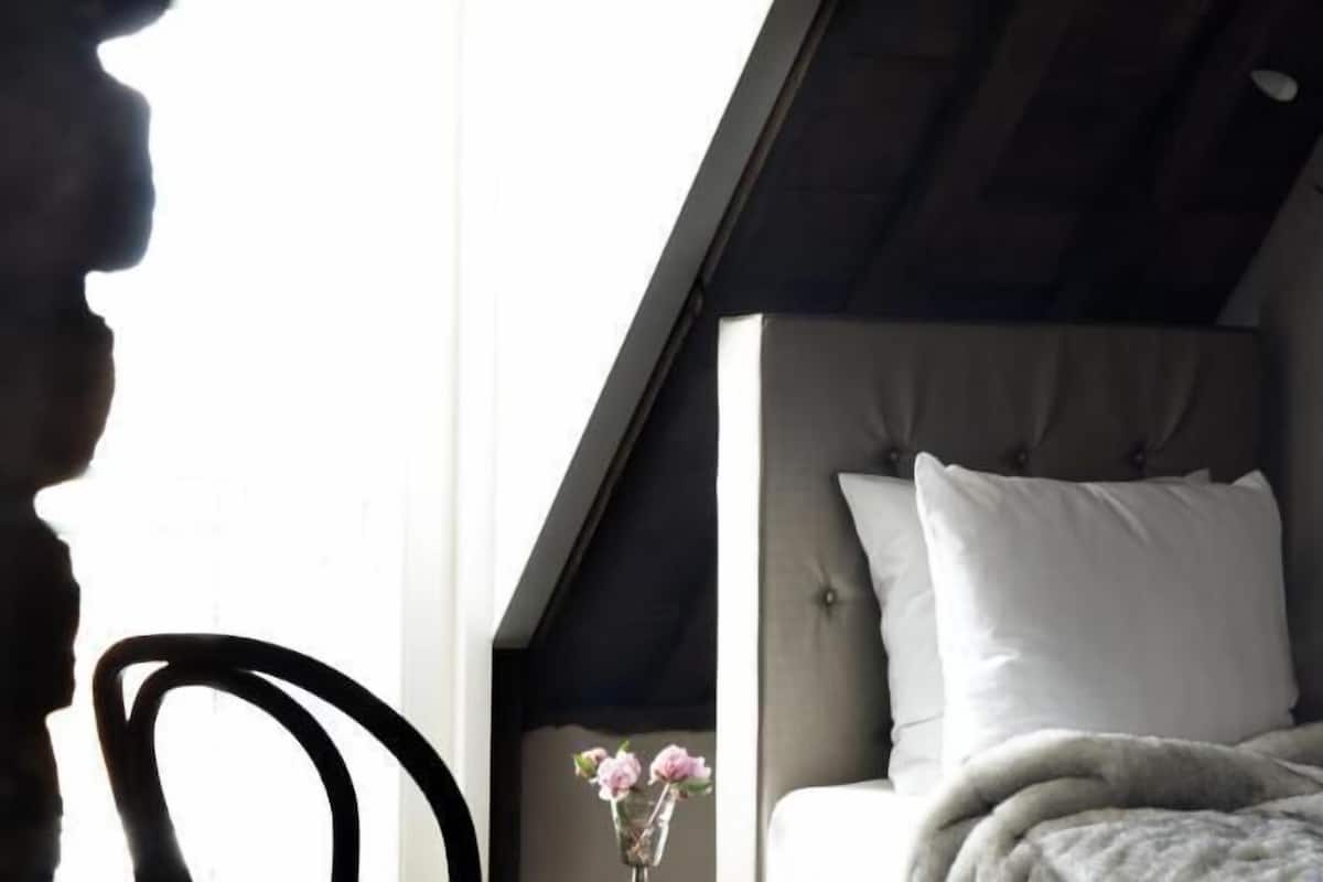 A bedroom with a bed, a chair, a vase with a flower, and a ceiling light fixture.