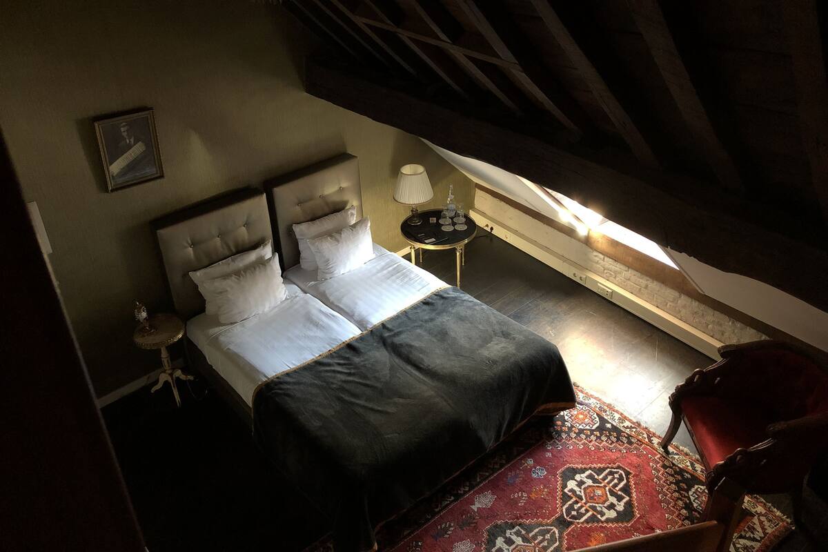 A bedroom with a bed, a nightstand, a lamp, a chair, and a patterned rug.