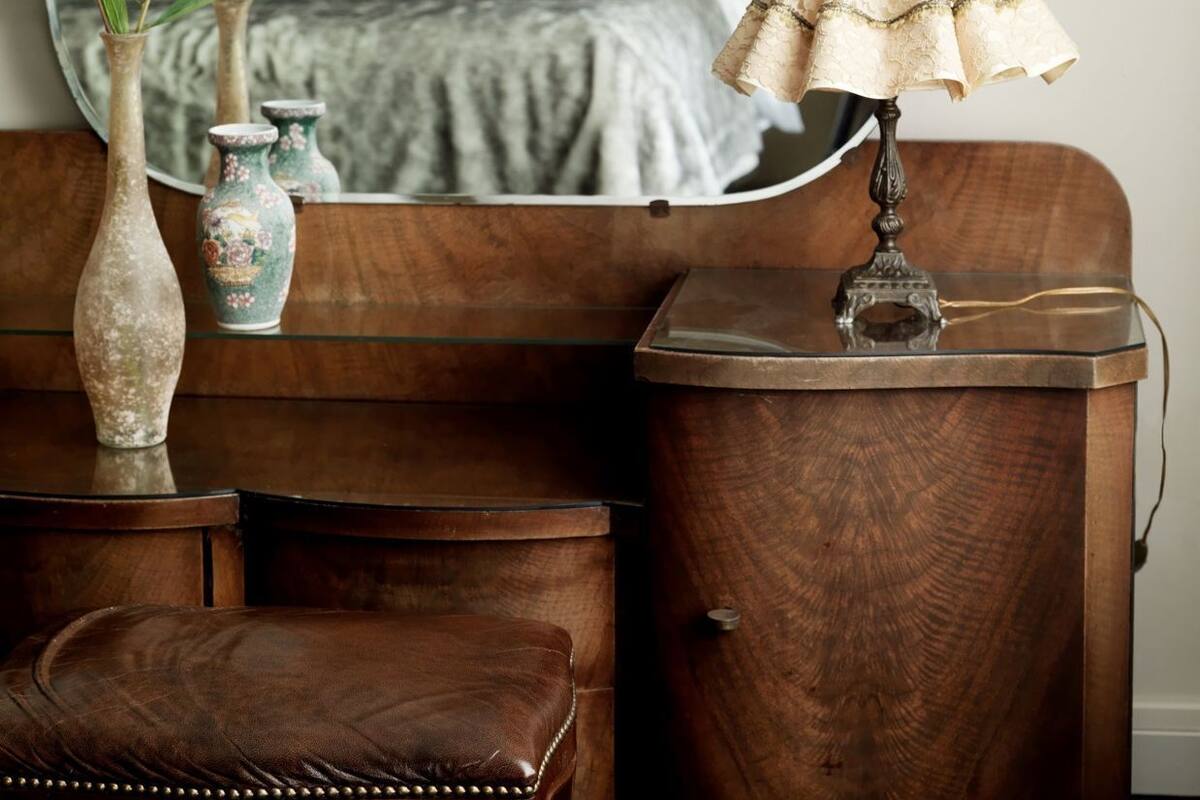 A bedroom with a bed, bedside table, lamp, and a mirror reflecting the room.