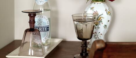 A bottle of mineral water, a glass with a drink, and a vase with red roses on a wooden table.