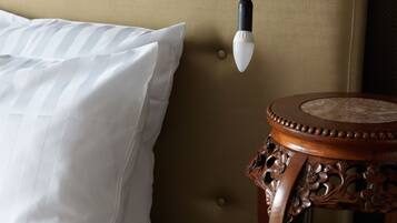 En säng med vita kuddar och en sänggavel, ett nattduksbord med en lampa och en vägg med en intressant yta.