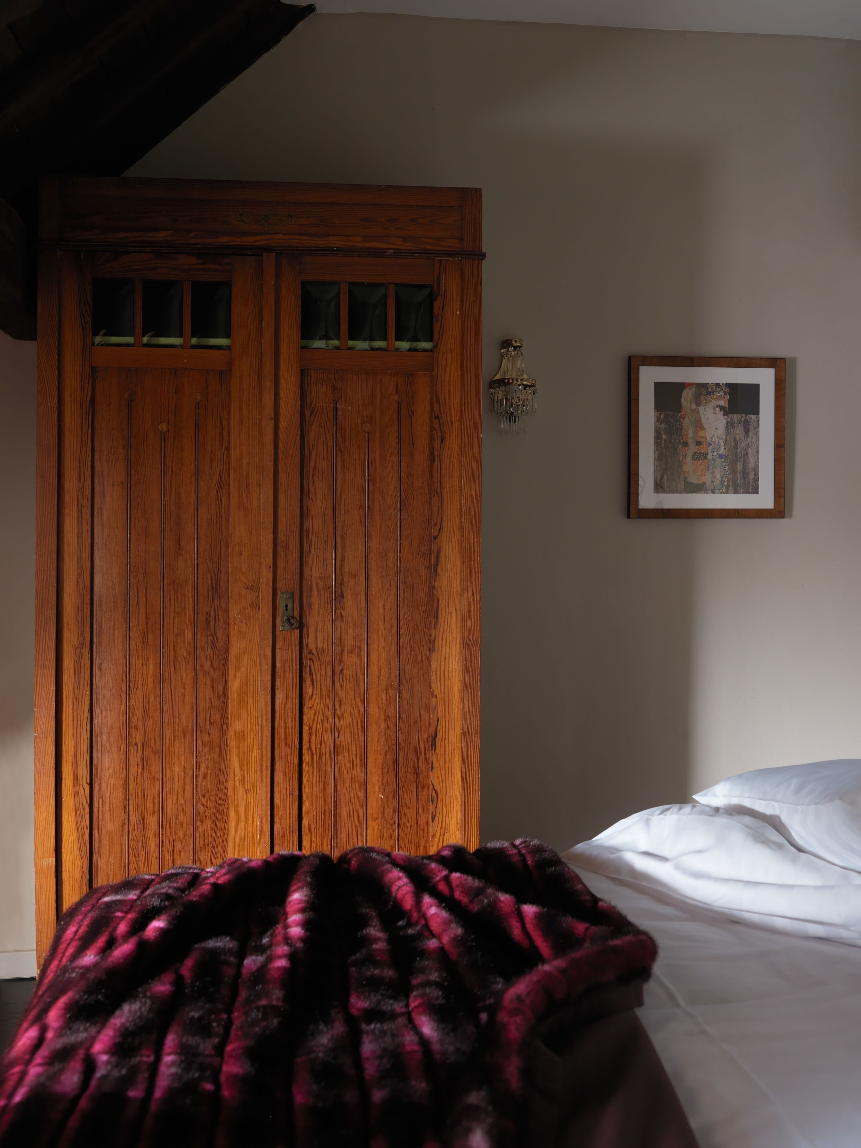 Una camera da letto con un armadio in legno, un letto con biancheria bianca e un quadro appeso al muro.