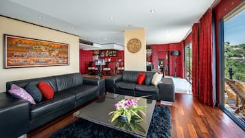 A modern living room with a black leather sofa, a glass coffee table with a flower arrangement, and a large painting on the wall.