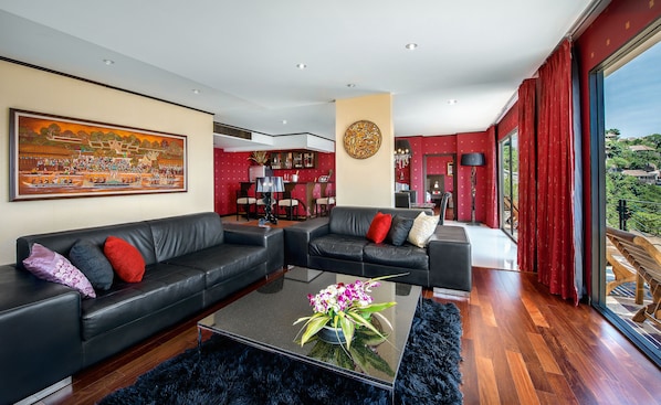A modern living room with a black leather sofa, a glass coffee table with a flower arrangement, and a large painting on the wall. - Jamahkiri Resort & Spa (Koh Tao)
