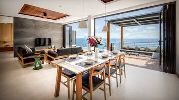 Ein modernes Wohnzimmer mit Fernseher, Sofa, Esstisch und Meerblick.