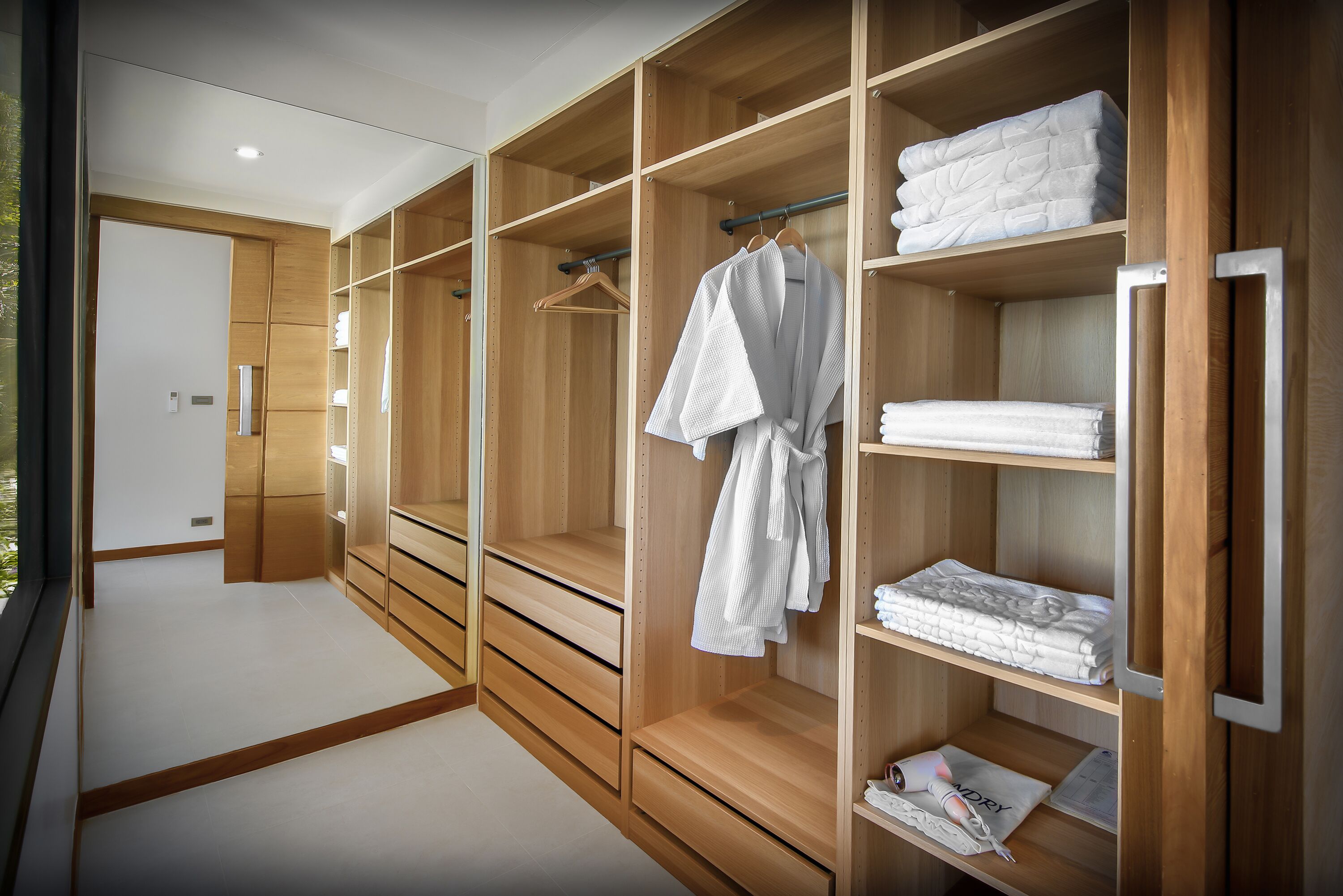 A walk-in closet with wooden shelving and drawers, containing neatly folded towels and a hanging robe.