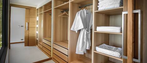 A walk-in closet with wooden shelving and drawers, containing neatly folded towels and a hanging robe.