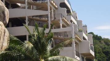 A multi-story building with balconies, surrounded by palm trees and rocks.