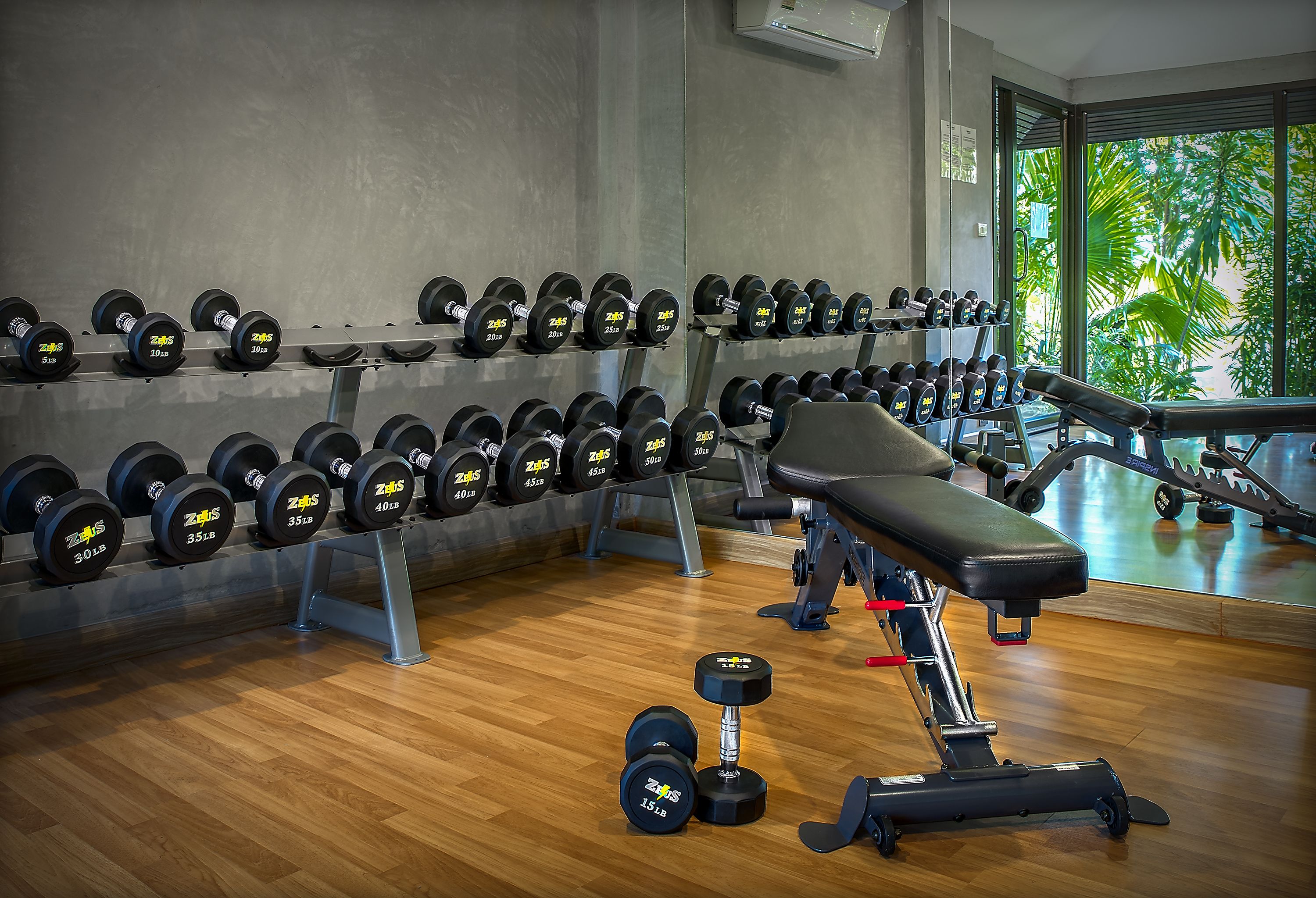 A gym with rows of dumbbells, a bench, and a mirror reflecting the room.