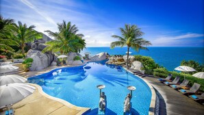 Una piscina con vista al océano, rodeada de palmeras y sillas de descanso.
