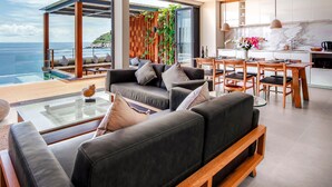 Una sala de estar moderna con piso de vidrio que da a un balcón con vista al mar, un comedor y una cocina con encimeras de mármol.