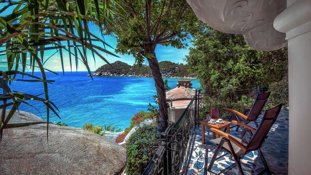 Una terraza con vista al mar, una mesa con sillas y un muro decorativo.