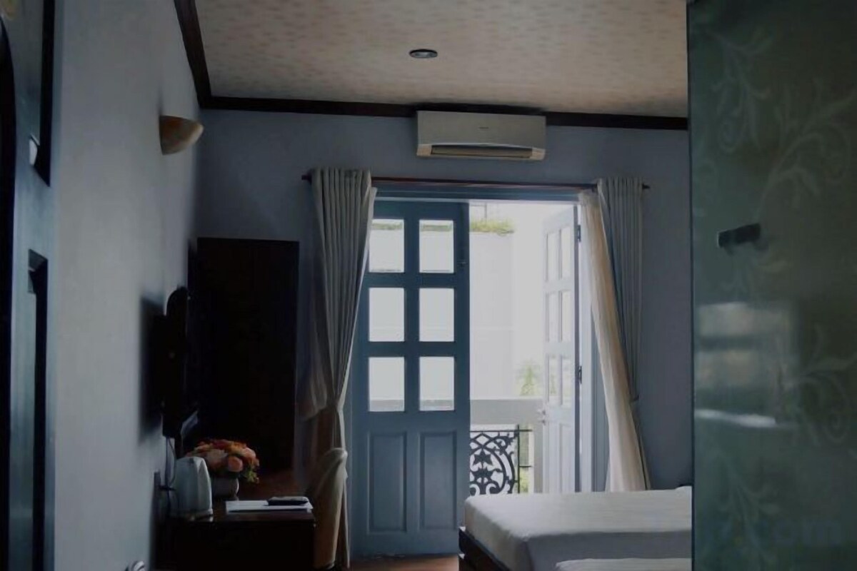 Una habitación de hotel con cama, escritorio con lámpara, televisión y ventana con cortinas.
