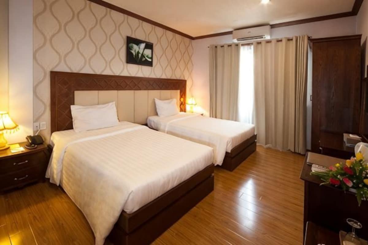 Une chambre d’hôtel avec deux lits, un plancher en bois, un grand miroir et un bureau agrémenté d’un vase de fleurs.