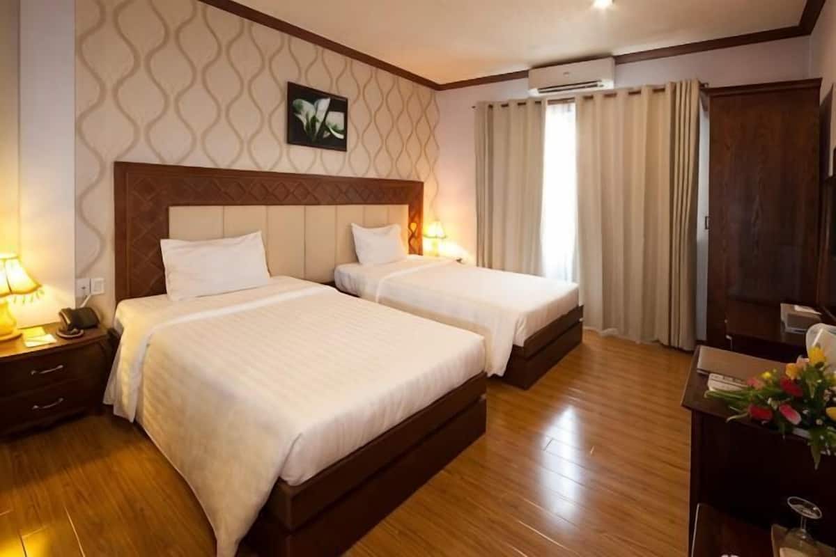 Une chambre d’hôtel avec deux lits, un plancher en bois, un grand miroir et un bureau agrémenté d’un vase de fleurs.