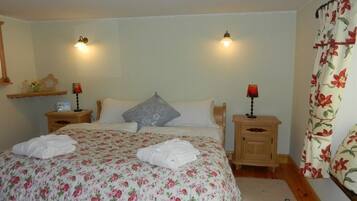 A bedroom with a floral bedspread, two bedside lamps, a nightstand with a radio, and a window with floral curtains.