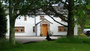 Un bâtiment blanc avec une porte en pierre et de nombreuses fenêtres, entouré d’arbres et d’herbe.