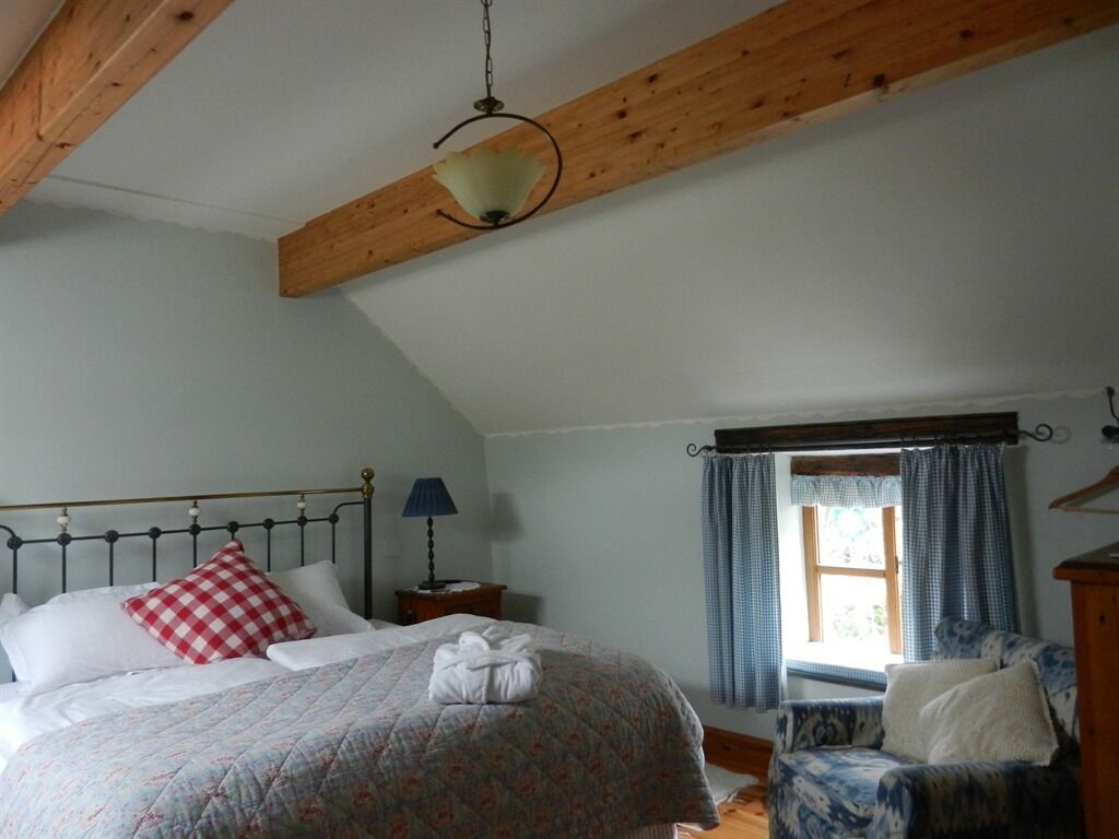A bedroom with a bed, a chair, a window with curtains, a lamp, and a hanging light fixture.