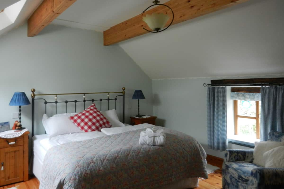 Ein Schlafzimmer mit einem Bett, zwei Nachttischlampen, einem Holzkopfende, einem Fenster mit Vorhängen und einem Holzboden.