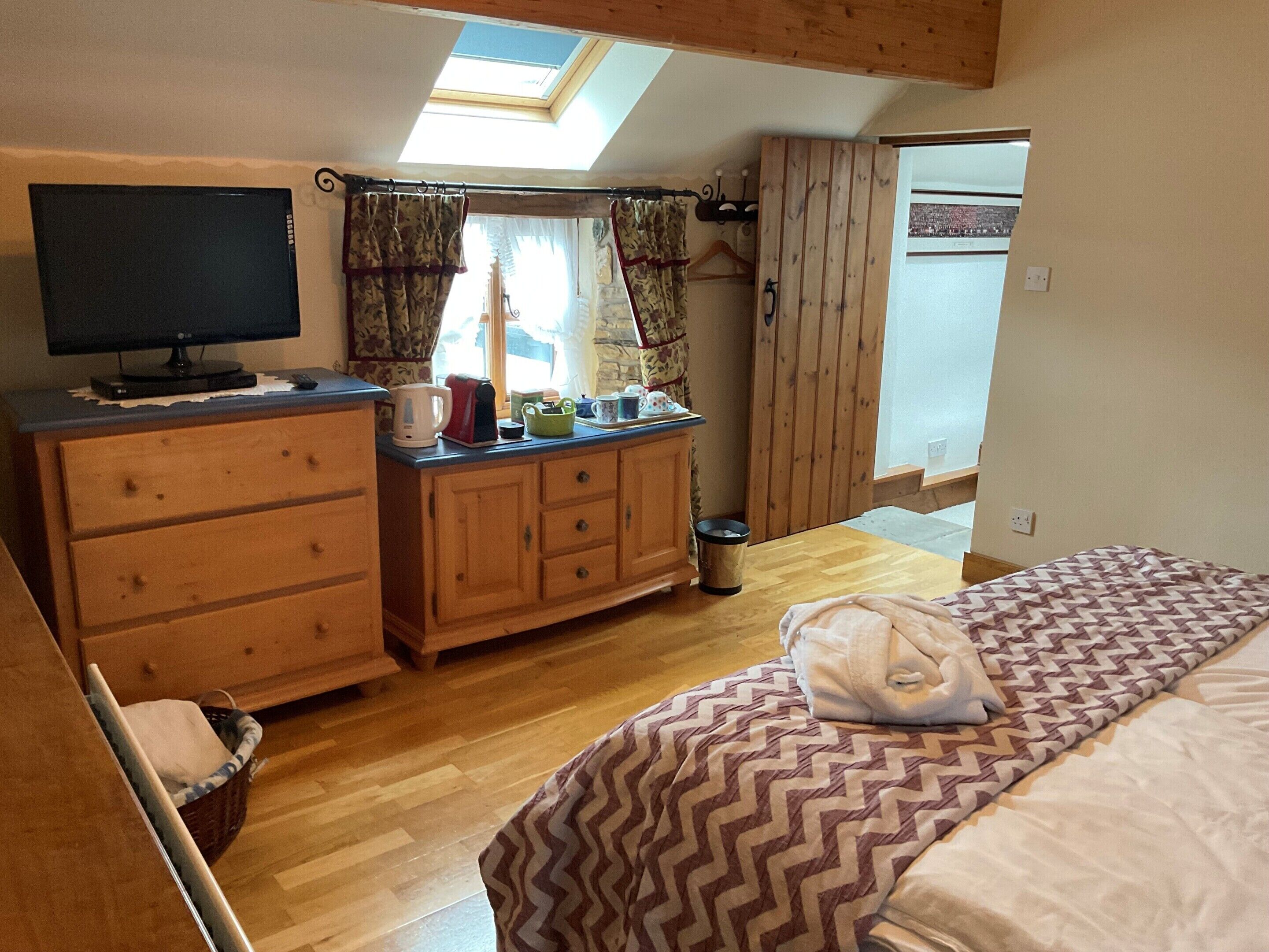 A cozy bedroom with a bed, a dresser, a television, and a skylight.