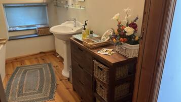 A bathroom with a white sink, wooden vanity, wicker baskets, a floral arrangement, and a window with a view.