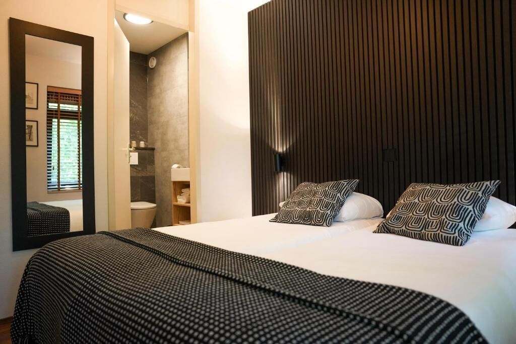 Een moderne slaapkamer met een groot bed, een spiegel, een kledingkast en een badkamer zichtbaar door een open deur.