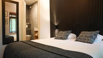 Een moderne slaapkamer met een groot bed, een spiegel, een kledingkast en een badkamer zichtbaar door een open deur.