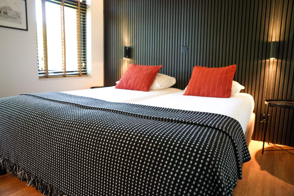 A neatly made bed with a black and white patterned bedspread and two red pillows.