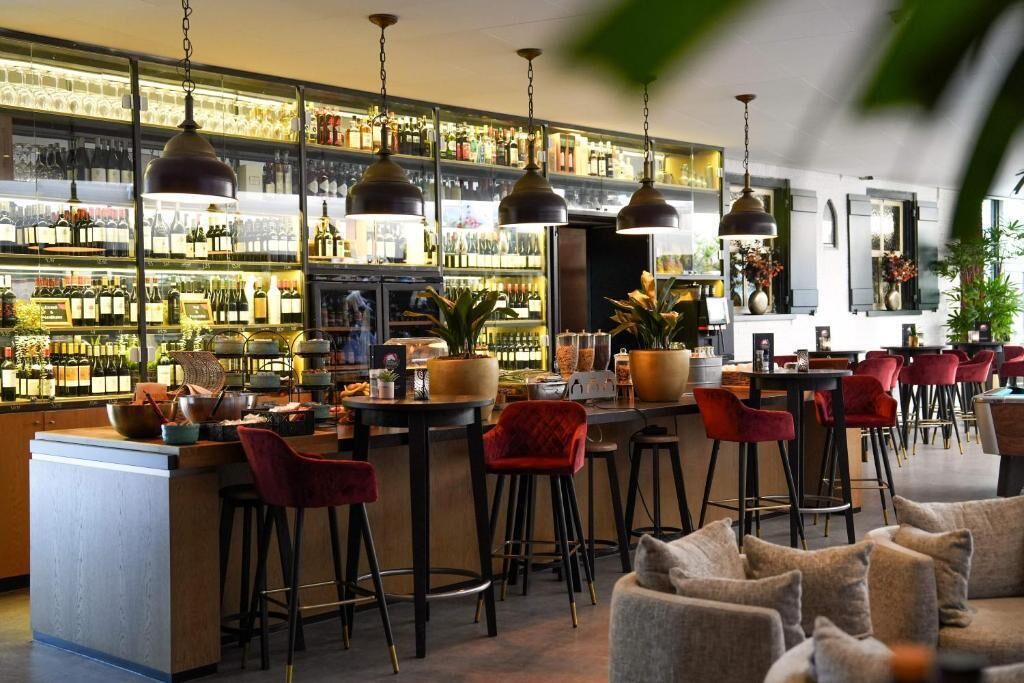 Zona de bar con varios taburetes, barra y estantes llenos de botellas.