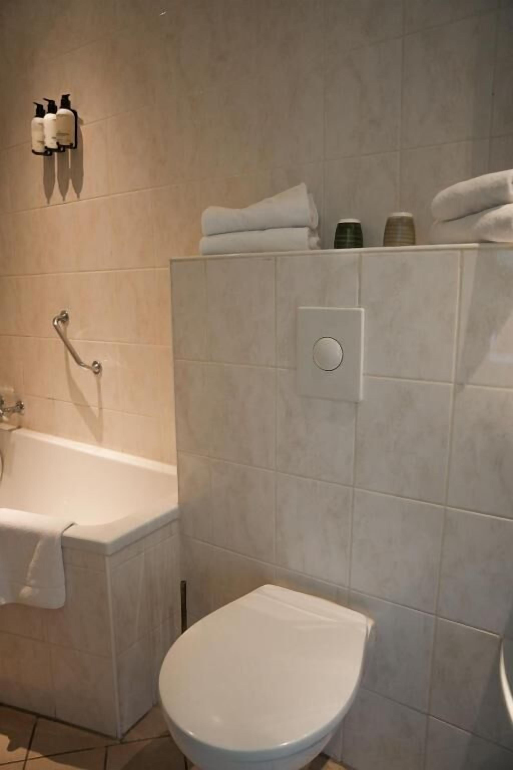 Een badkamer met een wit toilet, een bad met een handdoek en een douchekop aan de muur.