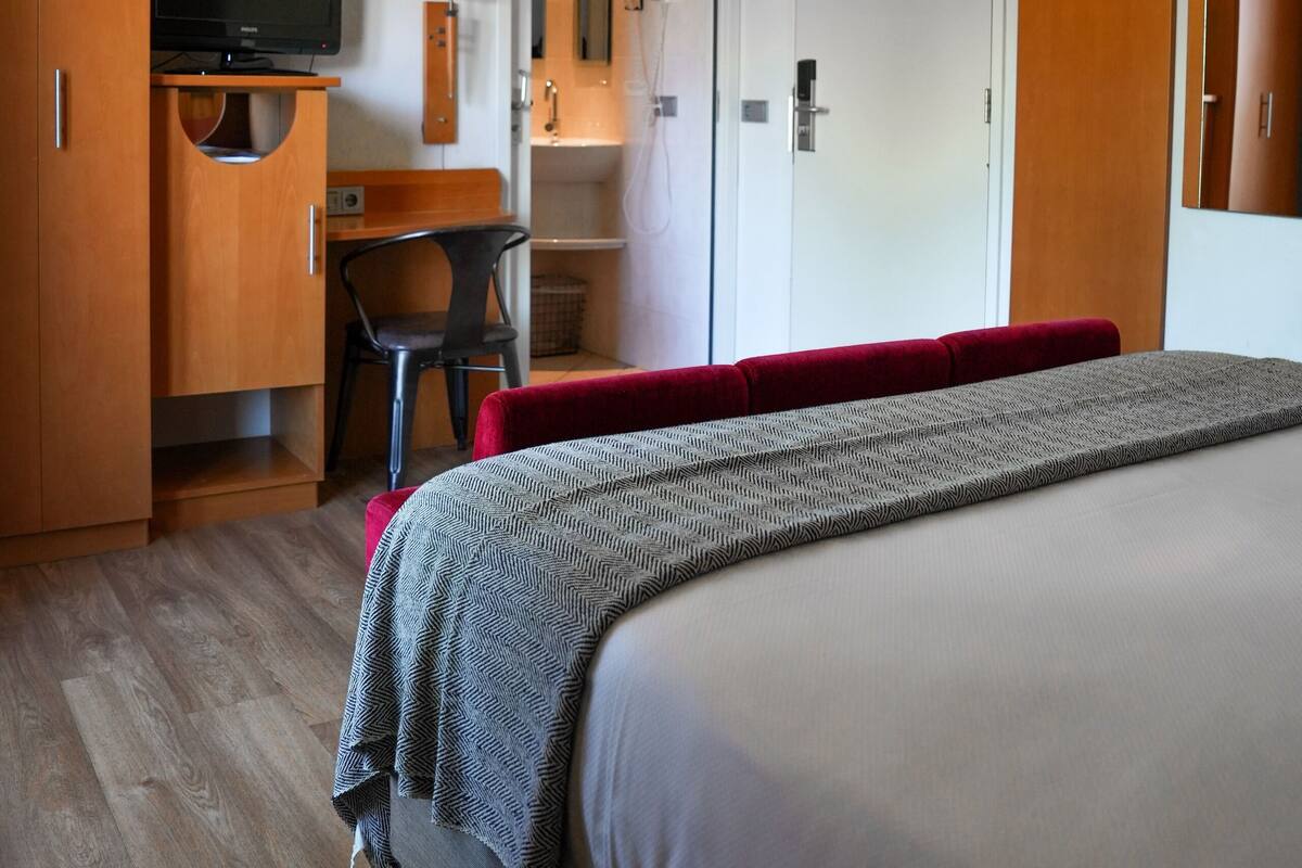 A hotel room with a bed, a desk, a television, and a wardrobe.