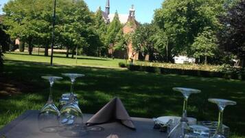 An outdoor dining table set with glasses, cutlery, and napkins, with a church and trees in the background.