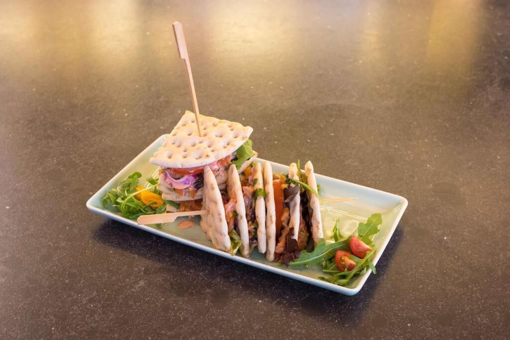 Ein rechteckiger Teller mit einem Sandwich, Salat und einem Stück Brot mit einem Zahnstocher.