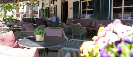 An outdoor seating area with wicker furniture, potted plants, and a view of the street.