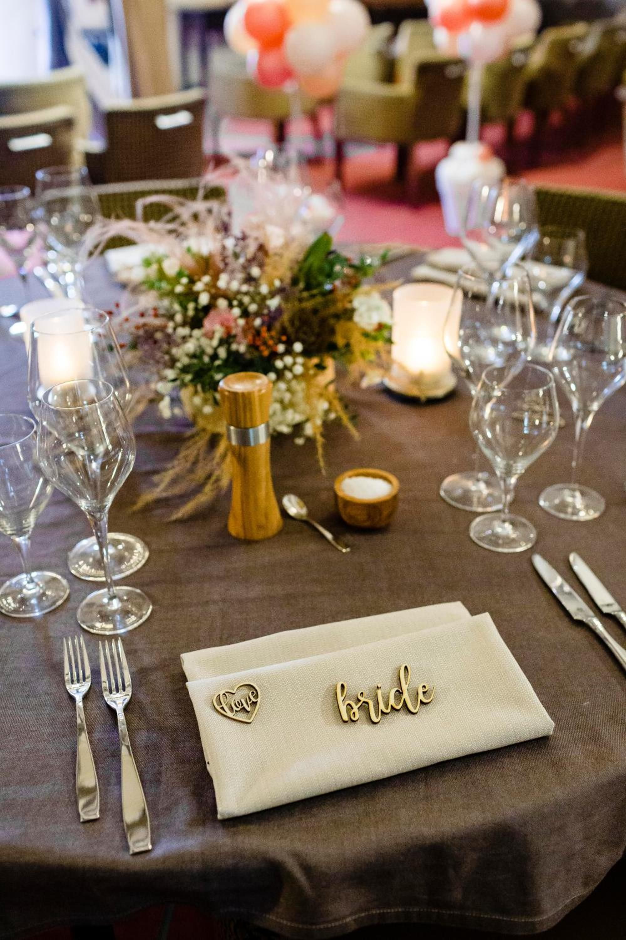 Una mesa dispuesta para una recepción de boda con servilleta con motivos nupciales, copas de vino, cubiertos y centros de mesa florales.