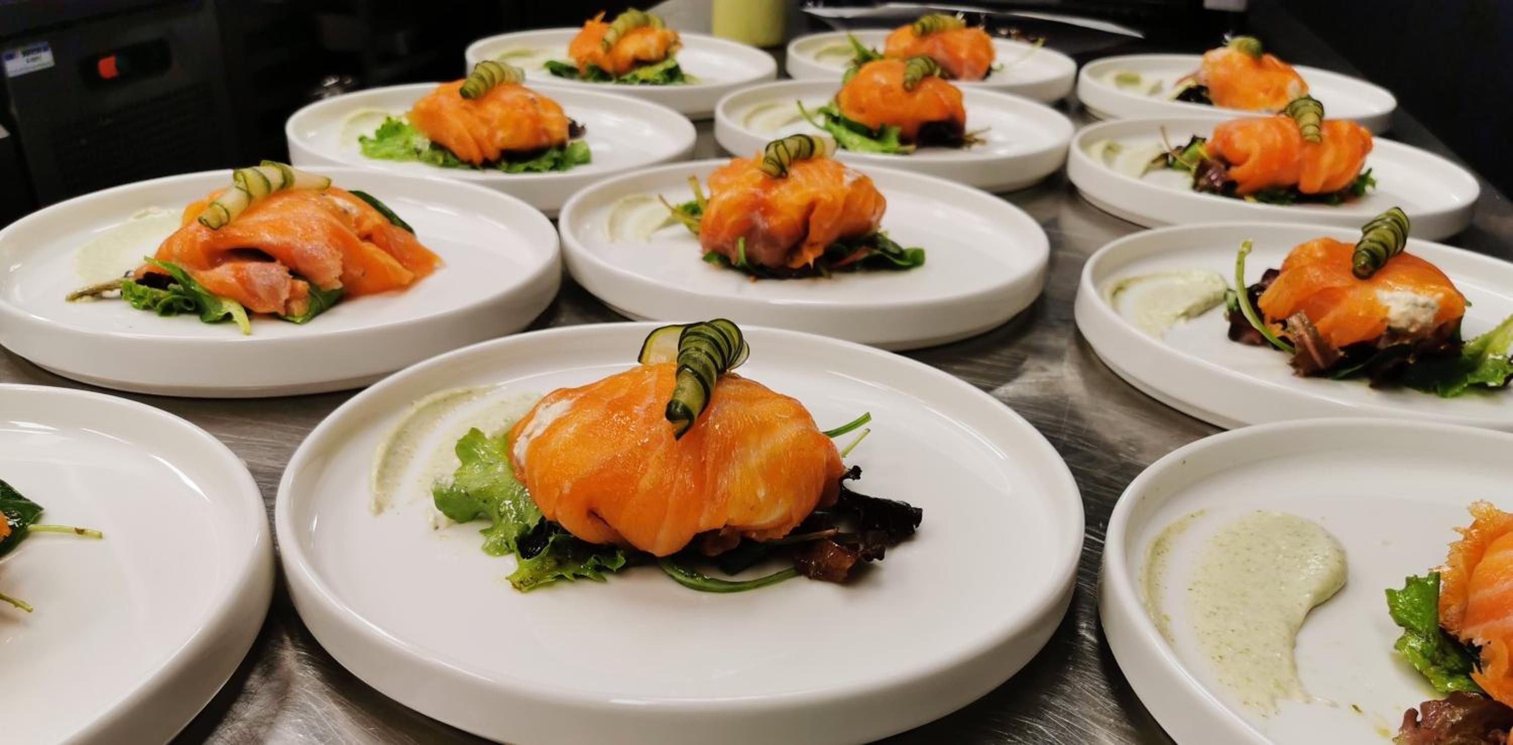 A series of white plates with salmon appetizers, garnished with green leaves and a decorative element.