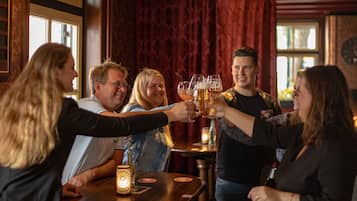 Een groep mensen die met bierglazen proosten in een bar met houten meubels en een kaars op tafel.