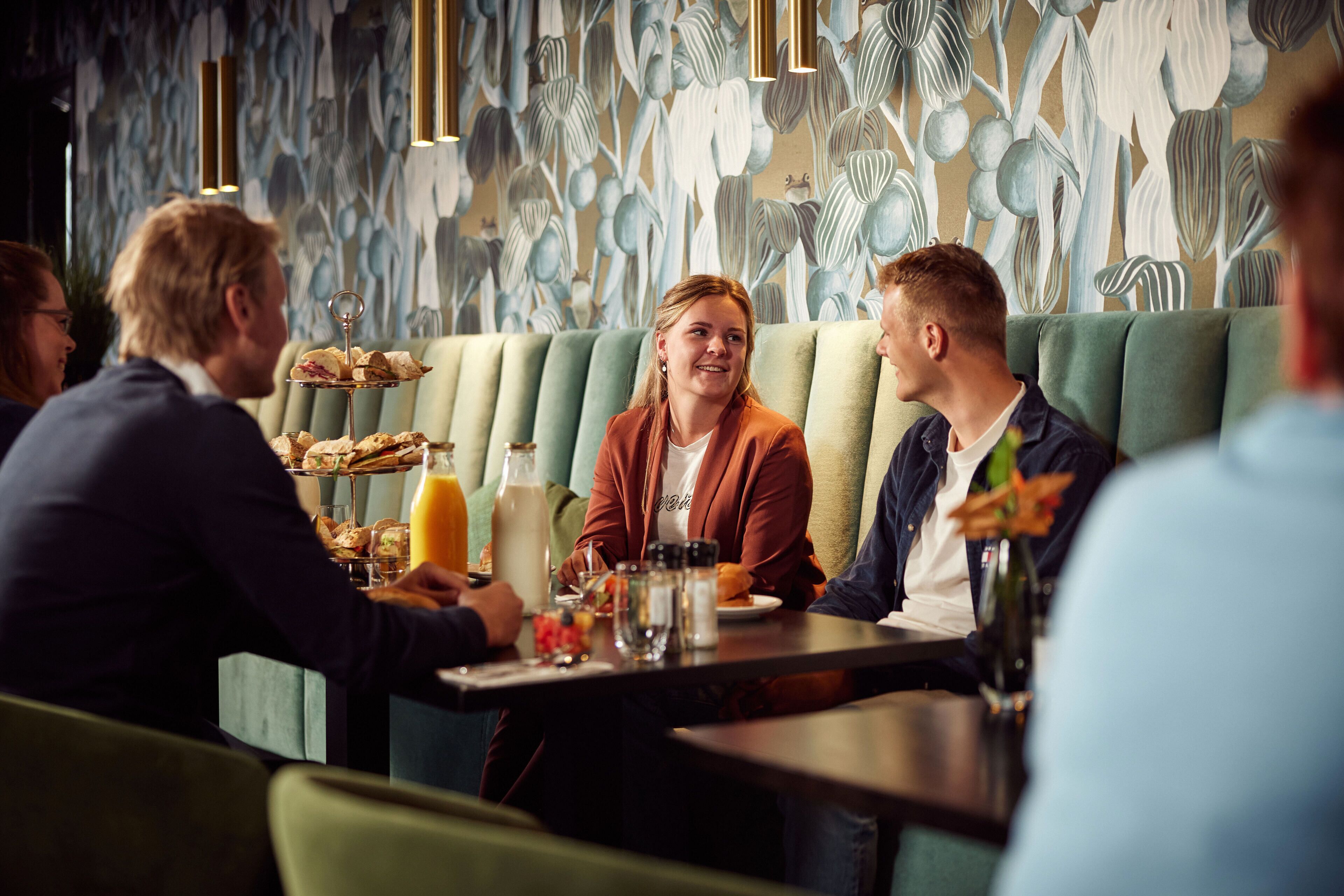 A restaurant with a modern interior, featuring a green cushioned booth seating area and a wall with a floral pattern.