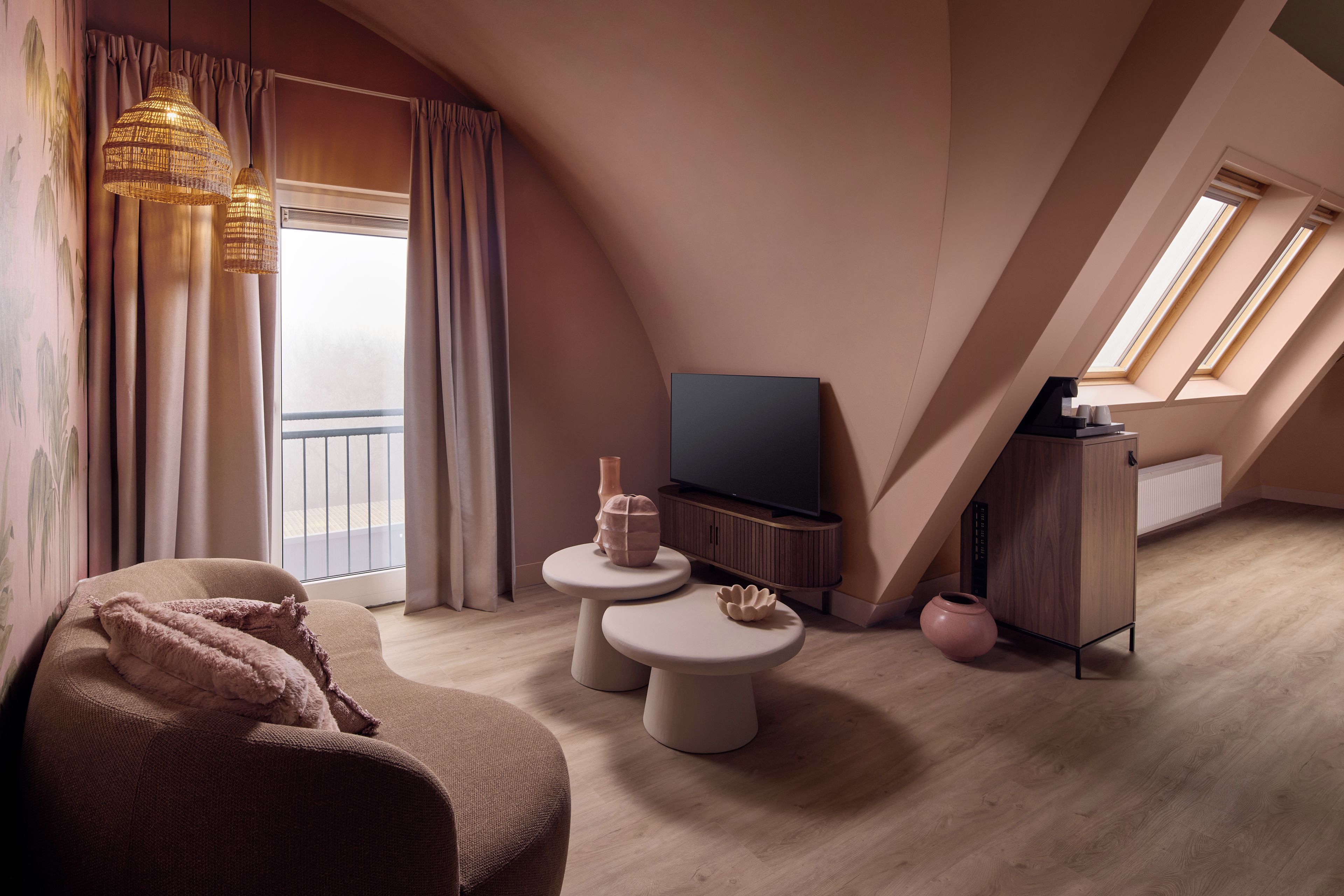 A modern loft bedroom with a large window, a flat-screen TV, a sofa, two side tables, and a decorative vase.