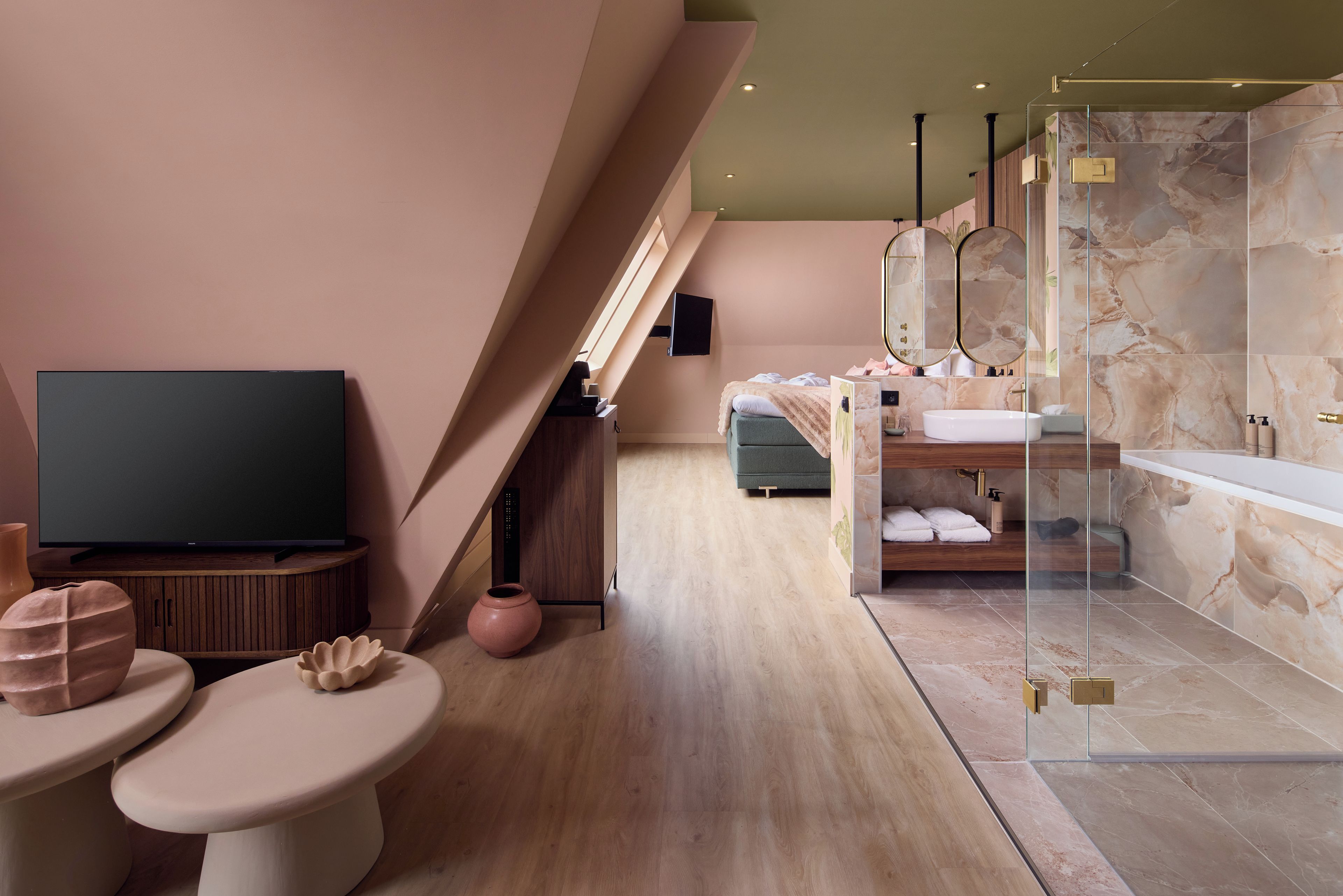 Une chambre d’hôtel moderne équipée d’une télévision, d’un canapé, d’une salle de bain avec baignoire et d’un grand miroir.