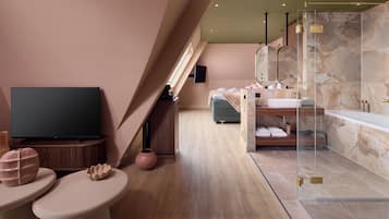 Une chambre d’hôtel moderne équipée d’une télévision, d’un canapé, d’une salle de bain avec baignoire et d’un grand miroir.
