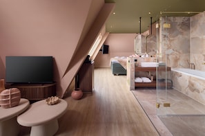 A modern hotel room with a television, a sofa, a bathroom with a bathtub, and a large mirror. - Van der Valk Hotel Texel (De Koog)