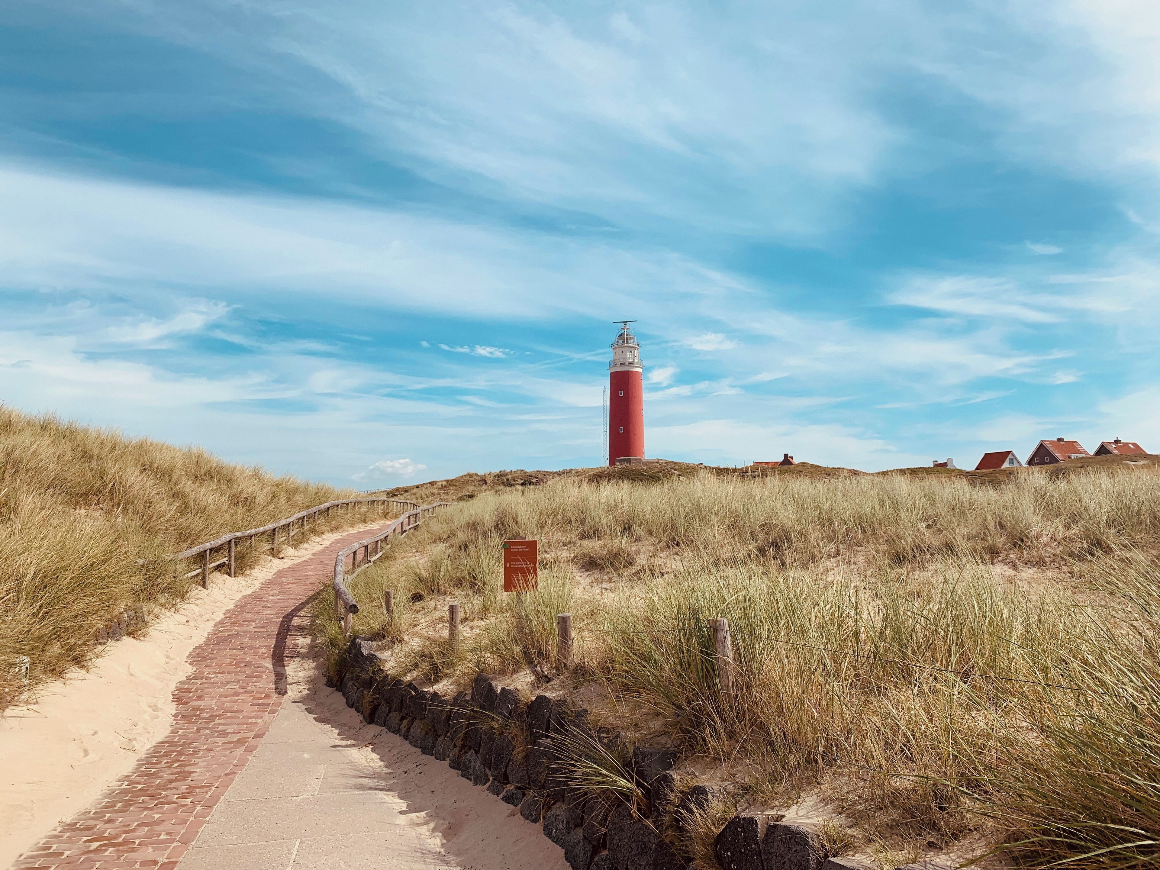 Un phare se dresse sur une colline herbeuse, et un chemin pavé de briques y mène.