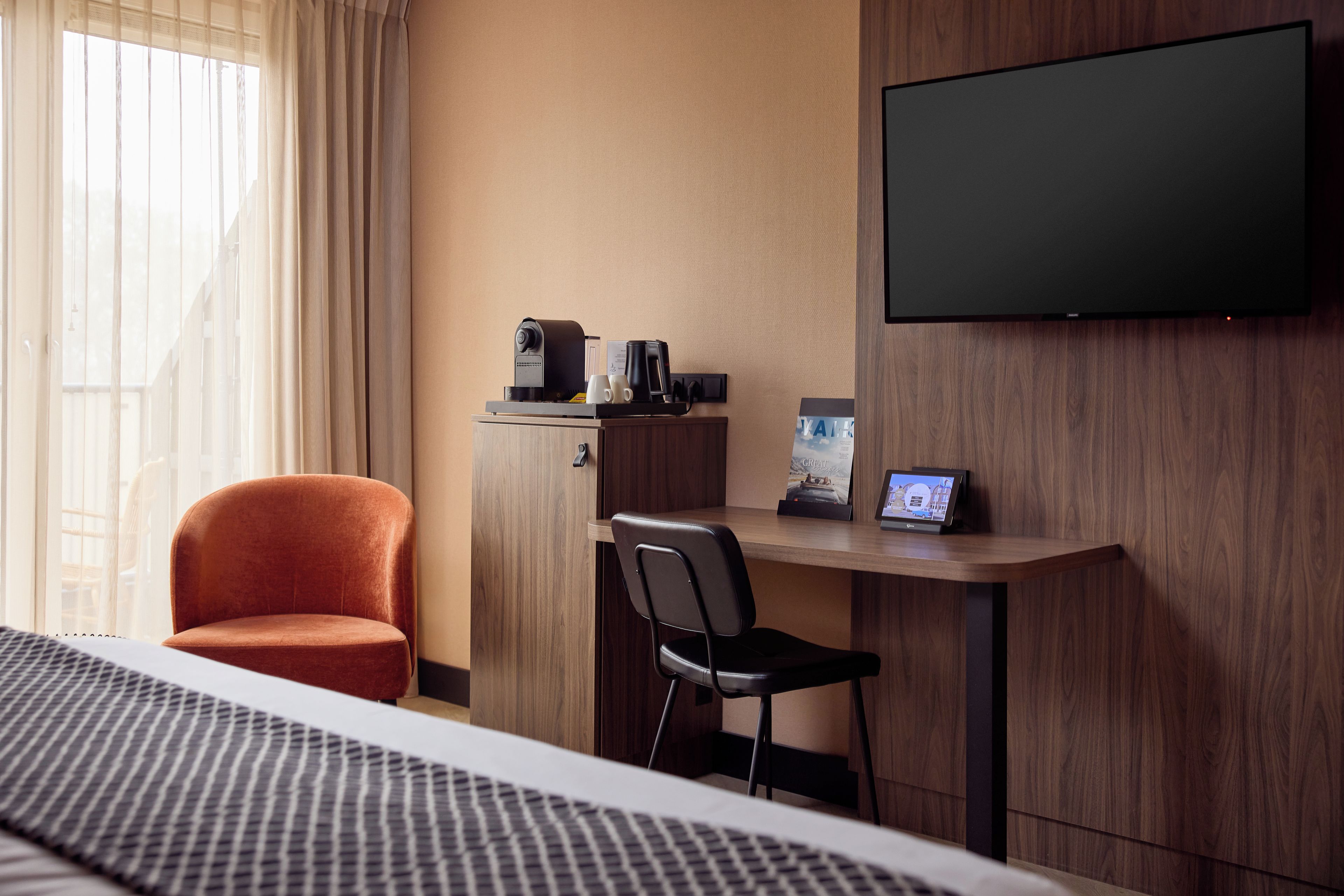 A hotel room with a bed, a desk with a coffee maker, a TV, and a chair.