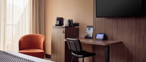 Una habitación de hotel con una cama, un escritorio con cafetera, un televisor y una silla.