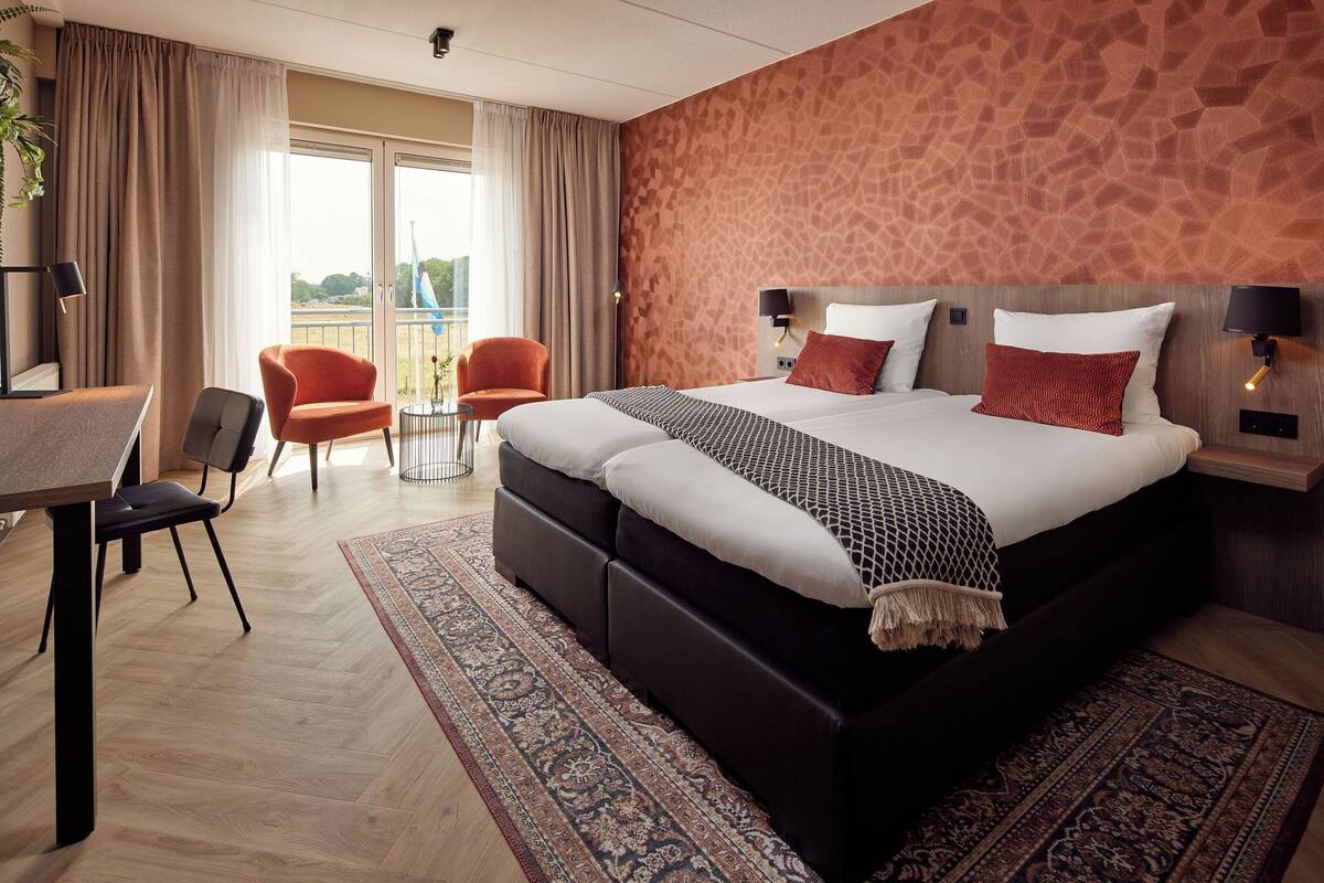 A modern hotel room with a large bed, a desk, a chair, and a balcony view.