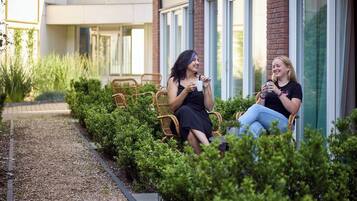 Two women sitting on wicker chairs in a garden area with a building in the background.