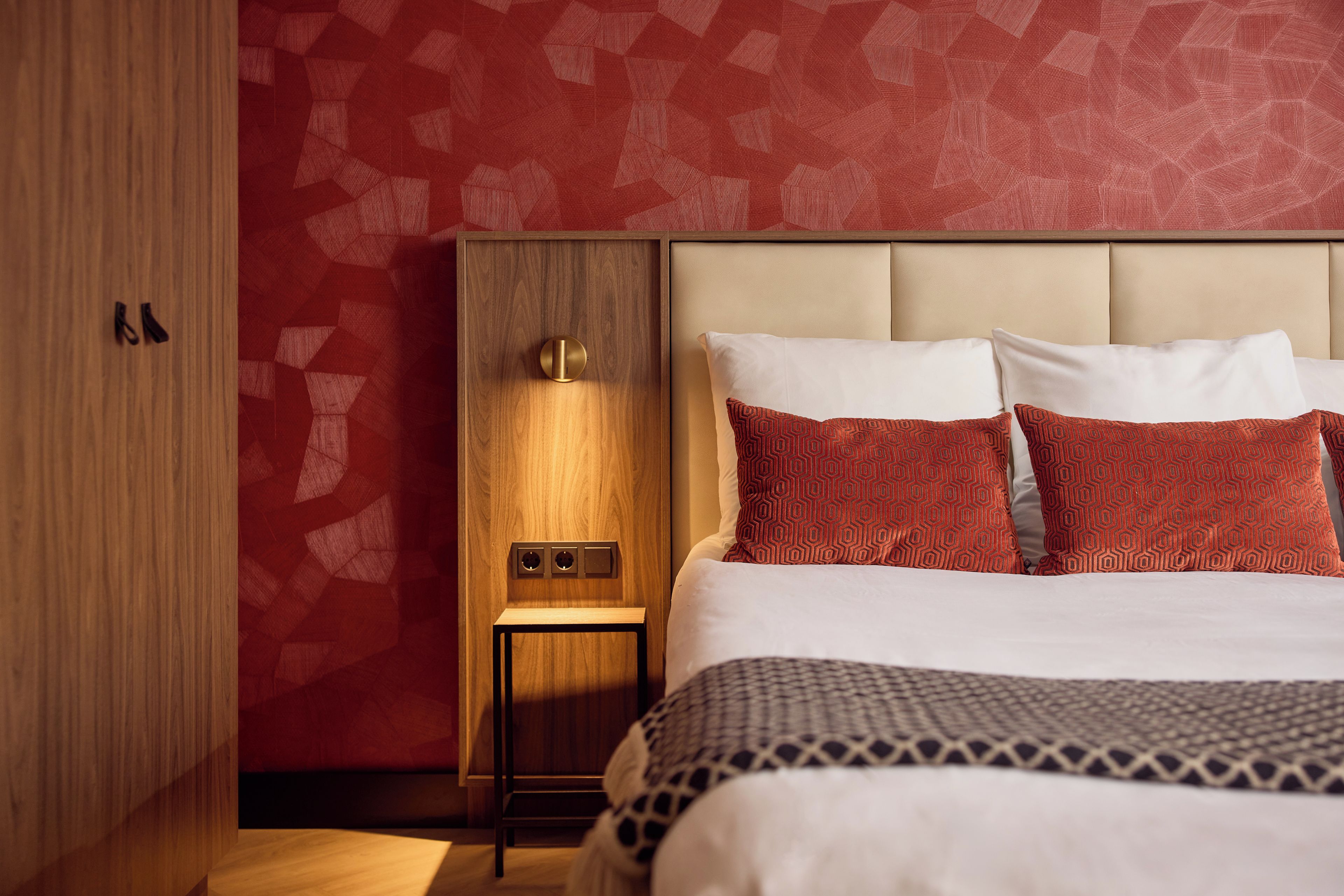 Een hotelkamer met een bed, een houten kledingkast, een nachtkastje en een wandlamp.