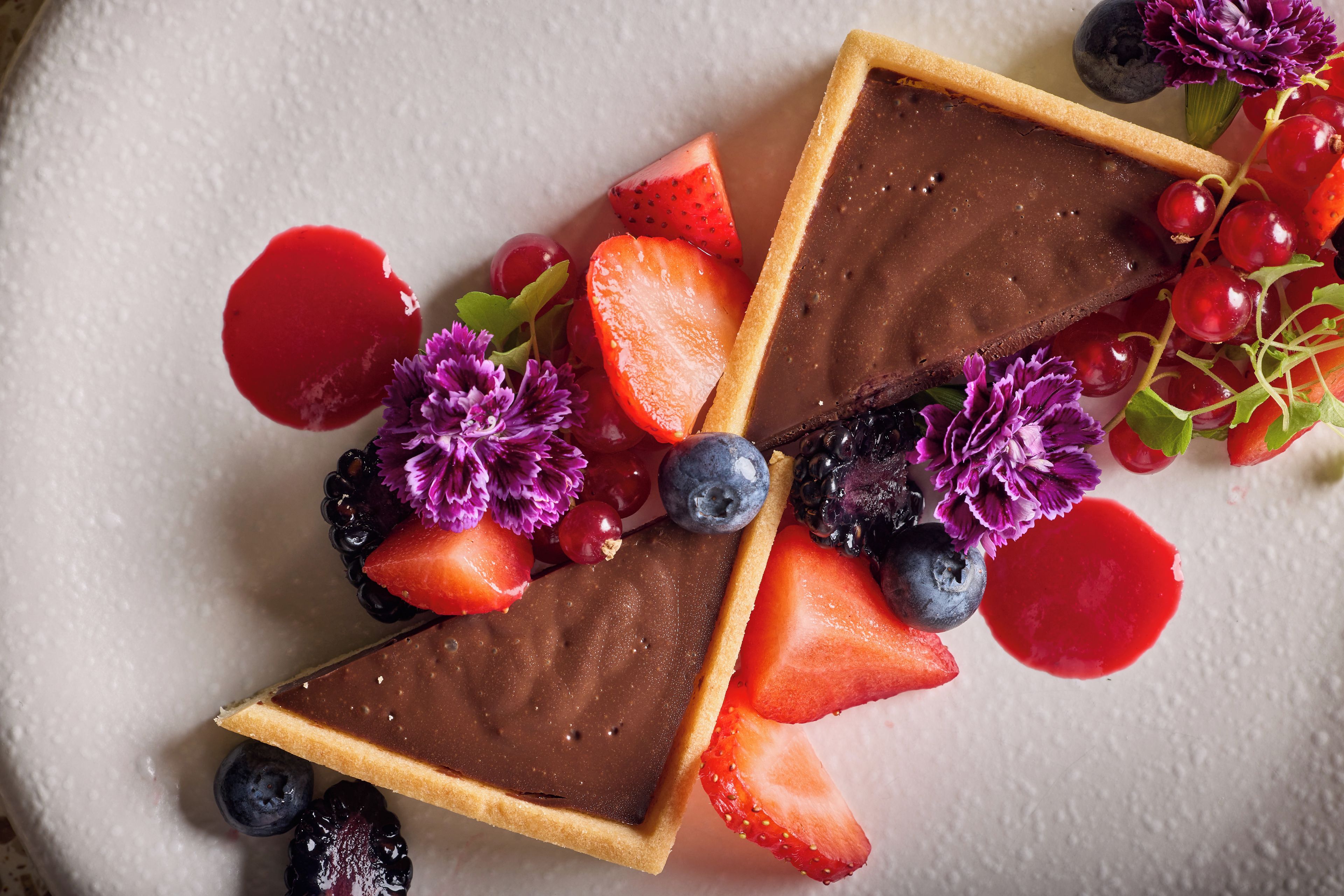 A dessert with chocolate, strawberries, blueberries, and flowers on a plate.